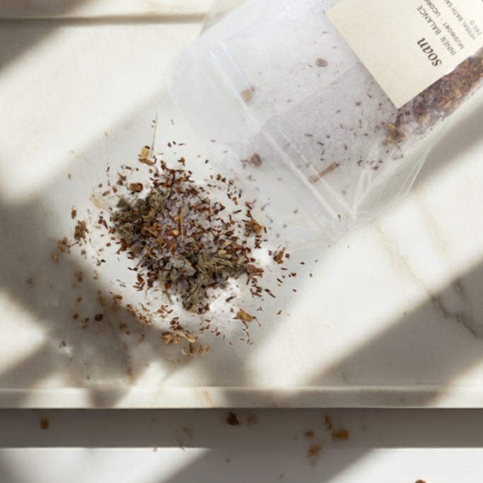 Tea leaves and bath salt on a marble surface with a herbal bath tea bag and packaging.