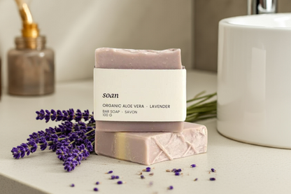 Two bars of soap with 'soan' branding on a bathroom counter with lavender flowers.