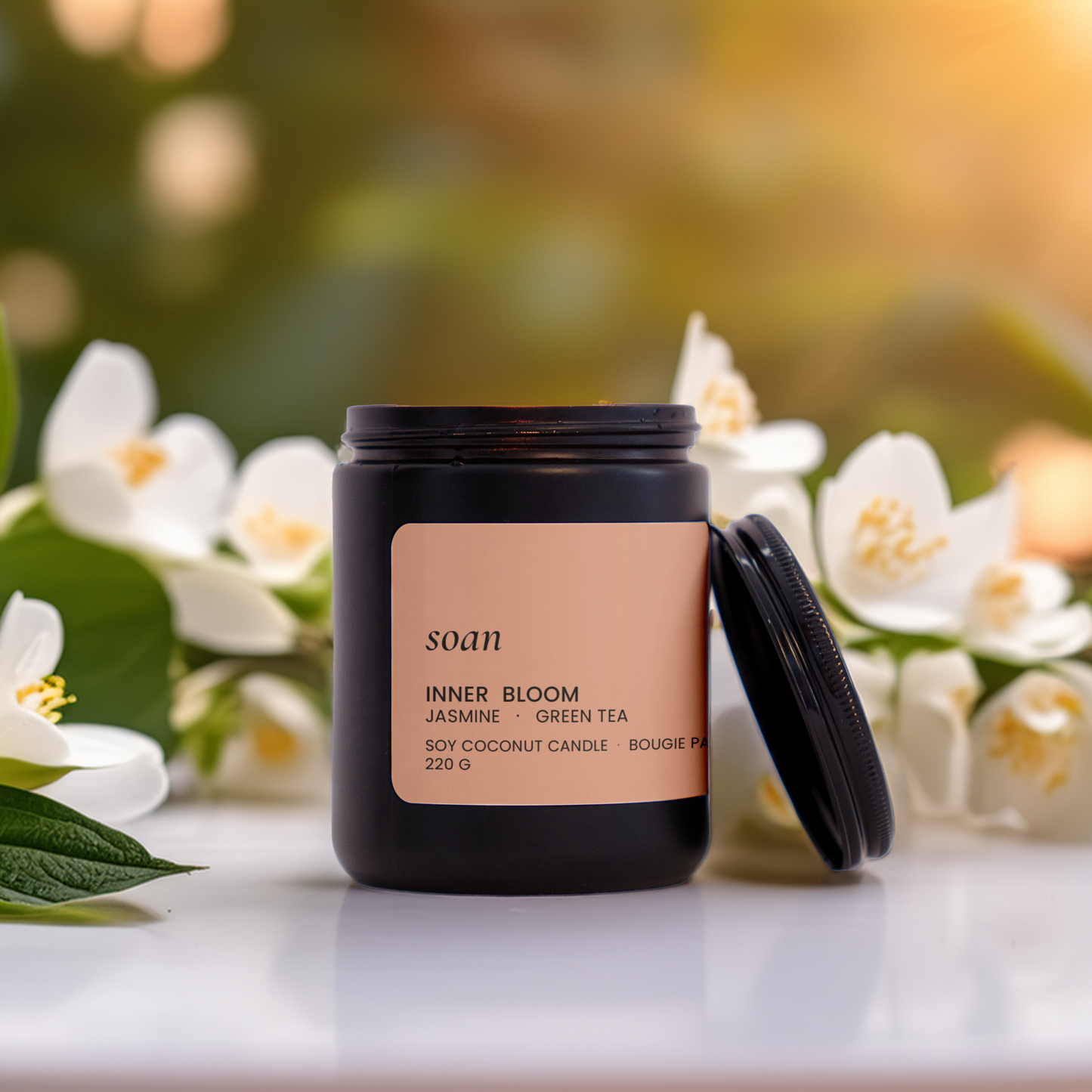 Candle labeled 'Inner Bloom' surrounded by jasmine flowers on a blurred natural background