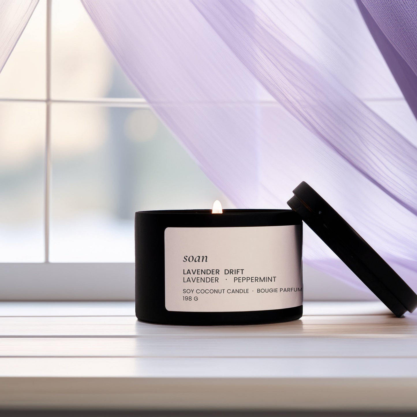 Scented candle with a label on a windowsill with purple curtains