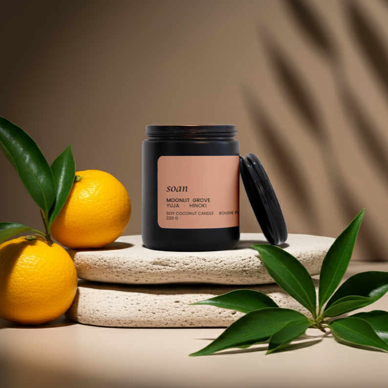 Candle with a pink label on a stone surface surrounded by oranges and leaves.
