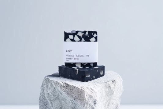 Black and white Charcoal soap bar with packaging on a stone surface against a light gray background