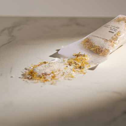 Bag of dried herbs and bath salt on a marble surface with a neutral background