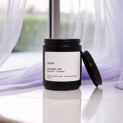 Candle with a label on a surface in front of sheer curtains