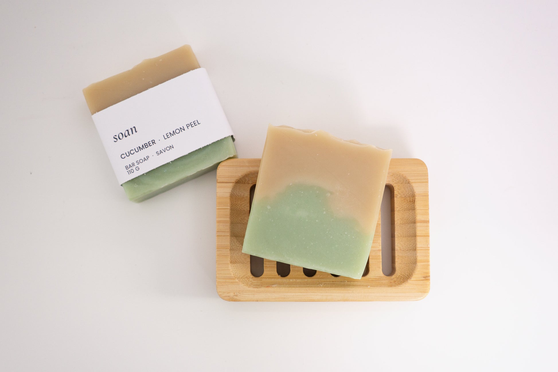 Two cucumber lemon bars of soap on a wooden soap dish with a white background