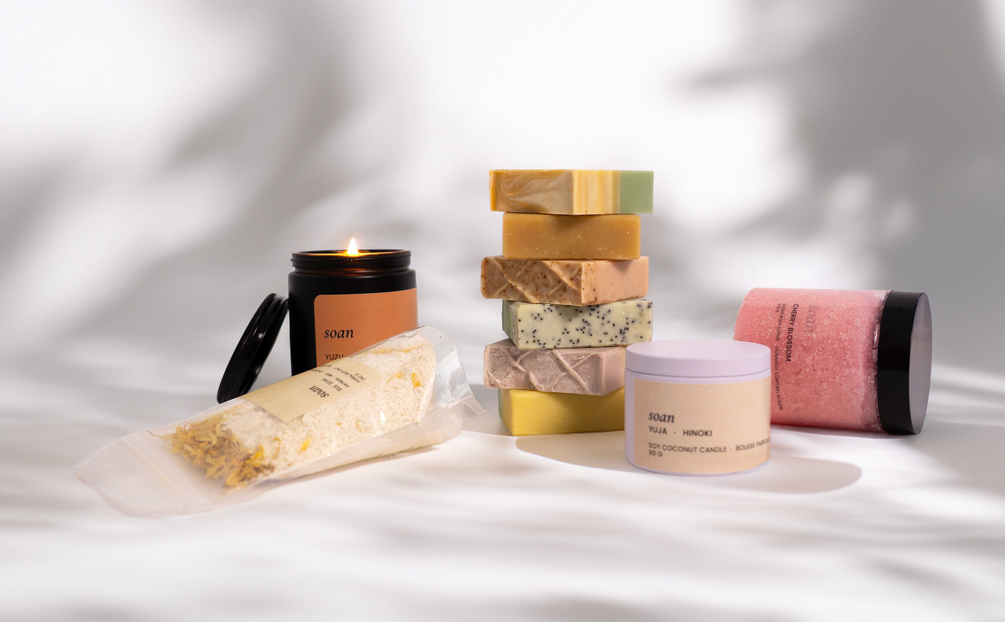 Collection of skincare products including bars, jars, and a candle on a soft white background