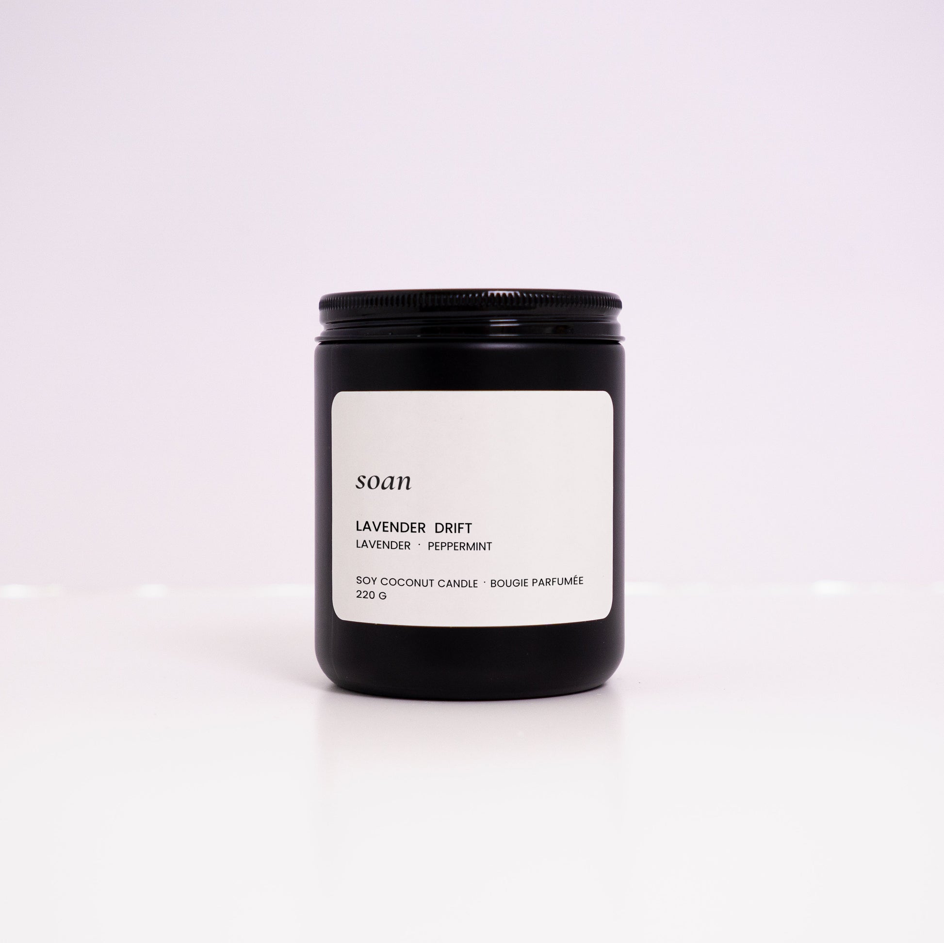 Black candle jar with a white label on a light purple background