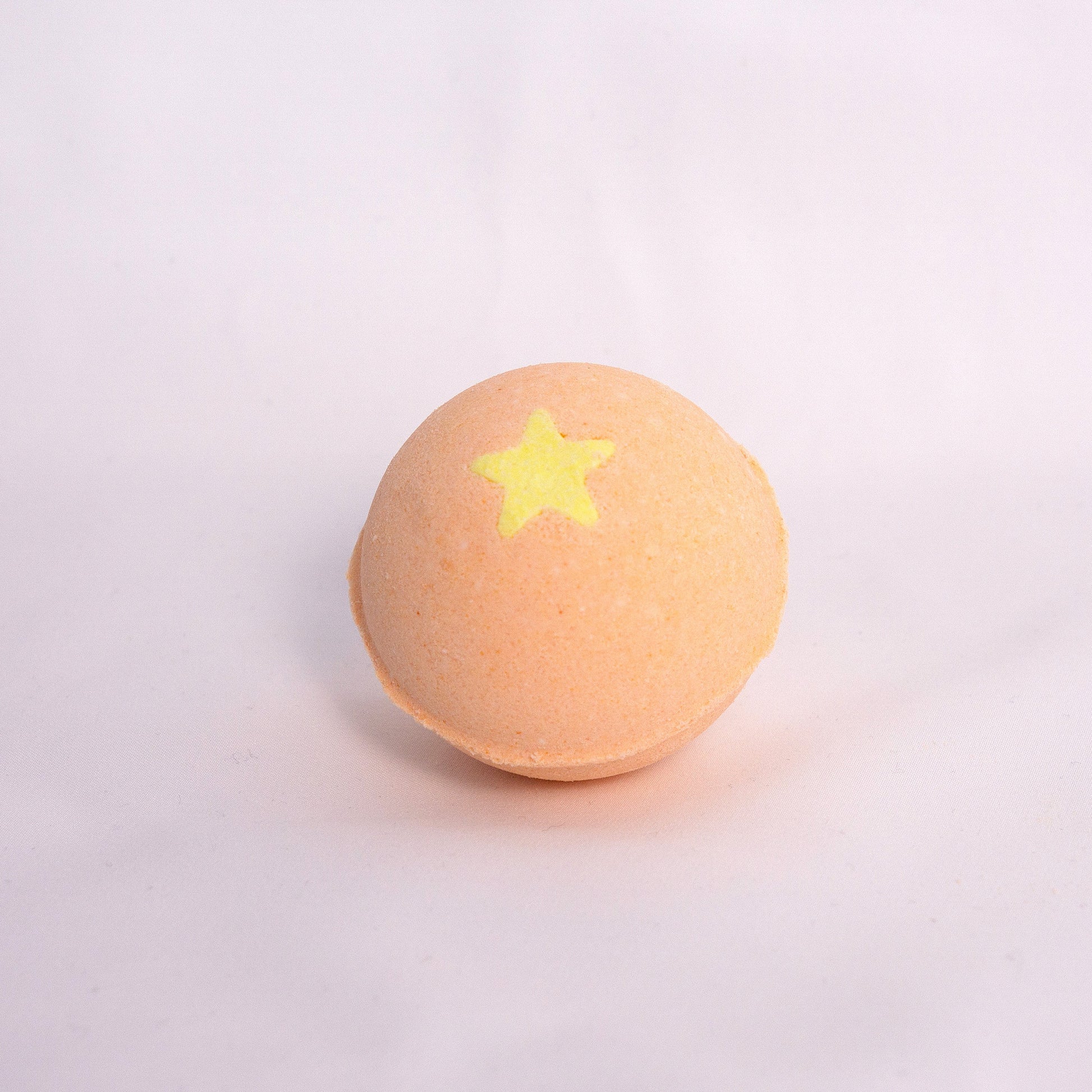 Close-up of Mango Bubble Bath Bomb on neutral surface, made with milk powder, shea butter, and avocado oil