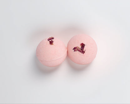 Two pink bath bombs with rose scent with rose petals on a light gray background