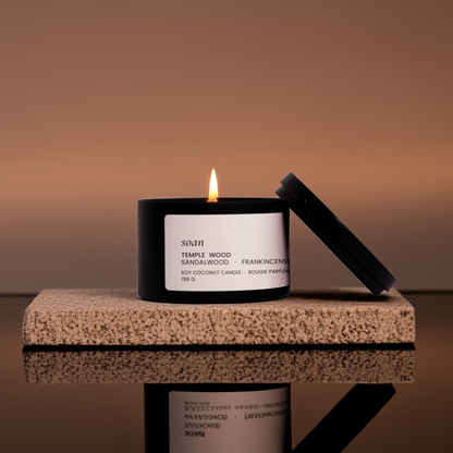 Candle with a black holder on a reflective surface against a brown background