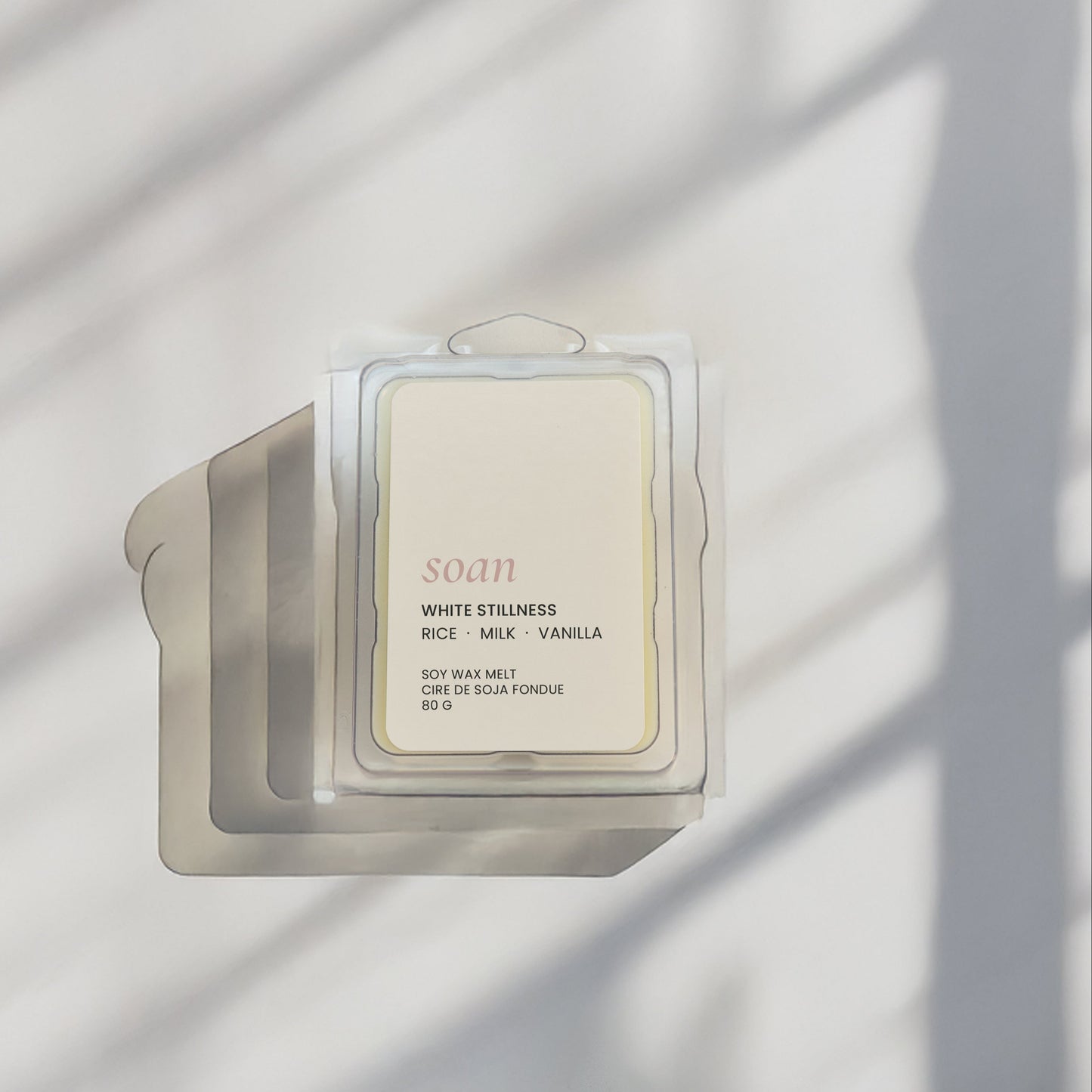 Candle with a label on a white surface with shadow patterns