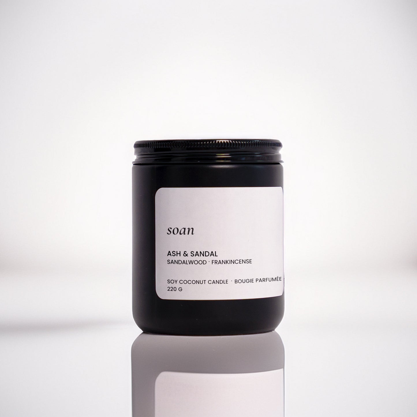 Candle jar labelled 'soan' on a reflective surface with a blurred background