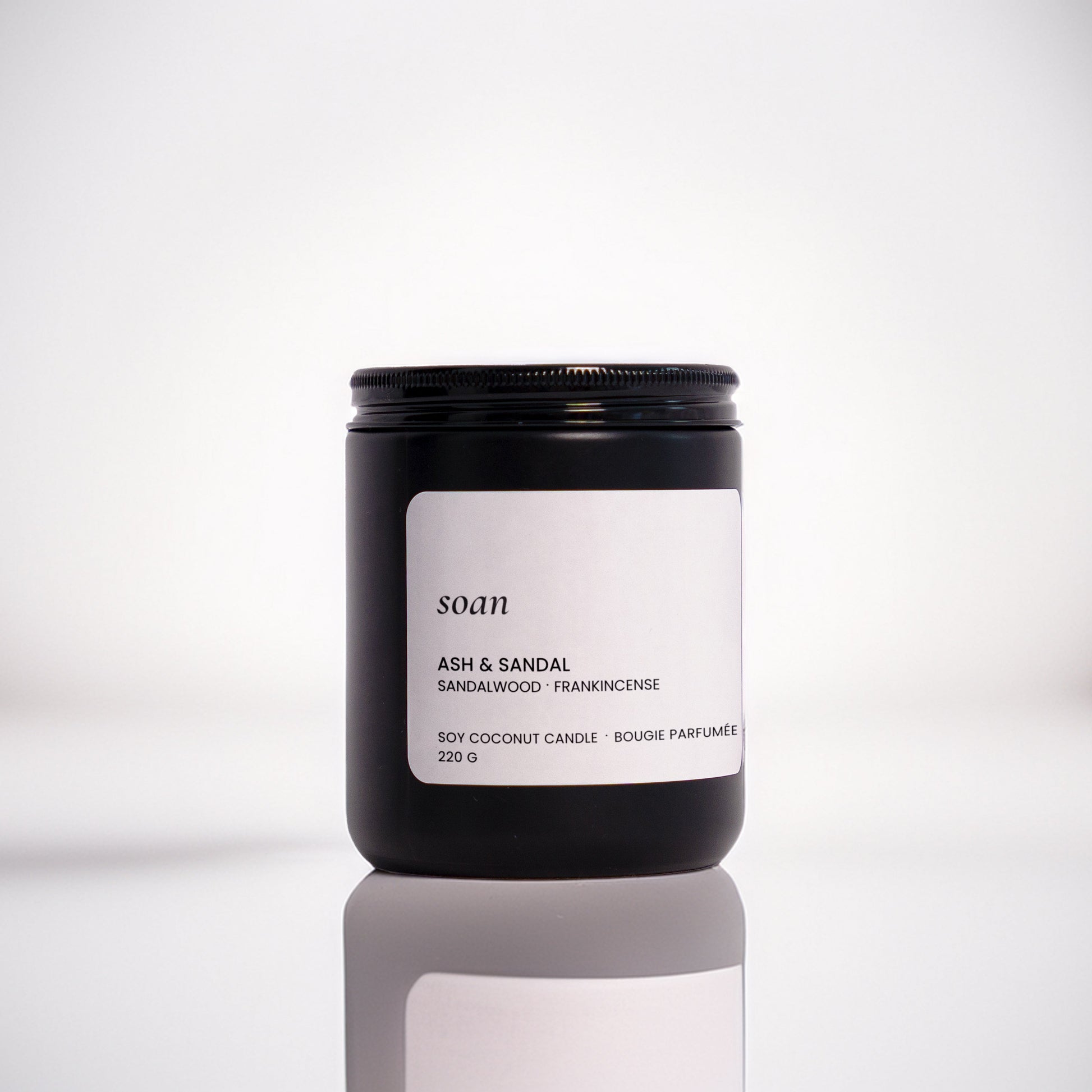 Candle jar labelled 'soan' on a reflective surface with a blurred background