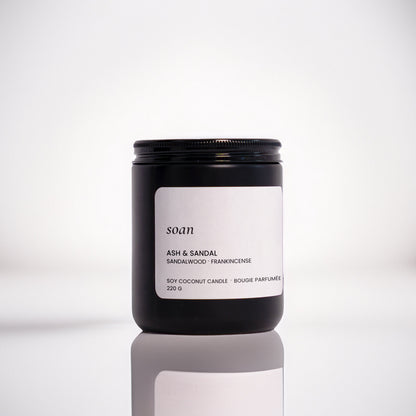 Candle jar labelled 'soan' on a reflective surface with a blurred background