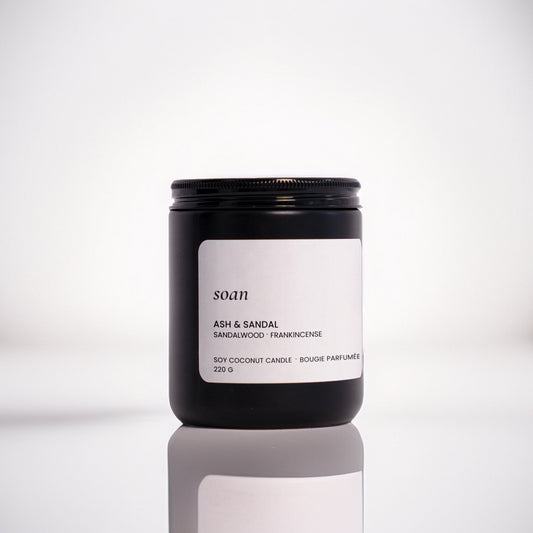 Candle jar labelled 'soan' on a reflective surface with a blurred background