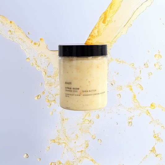 Jar of Sugar Body Scrub with a splash of yellow liquid against a light blue background
