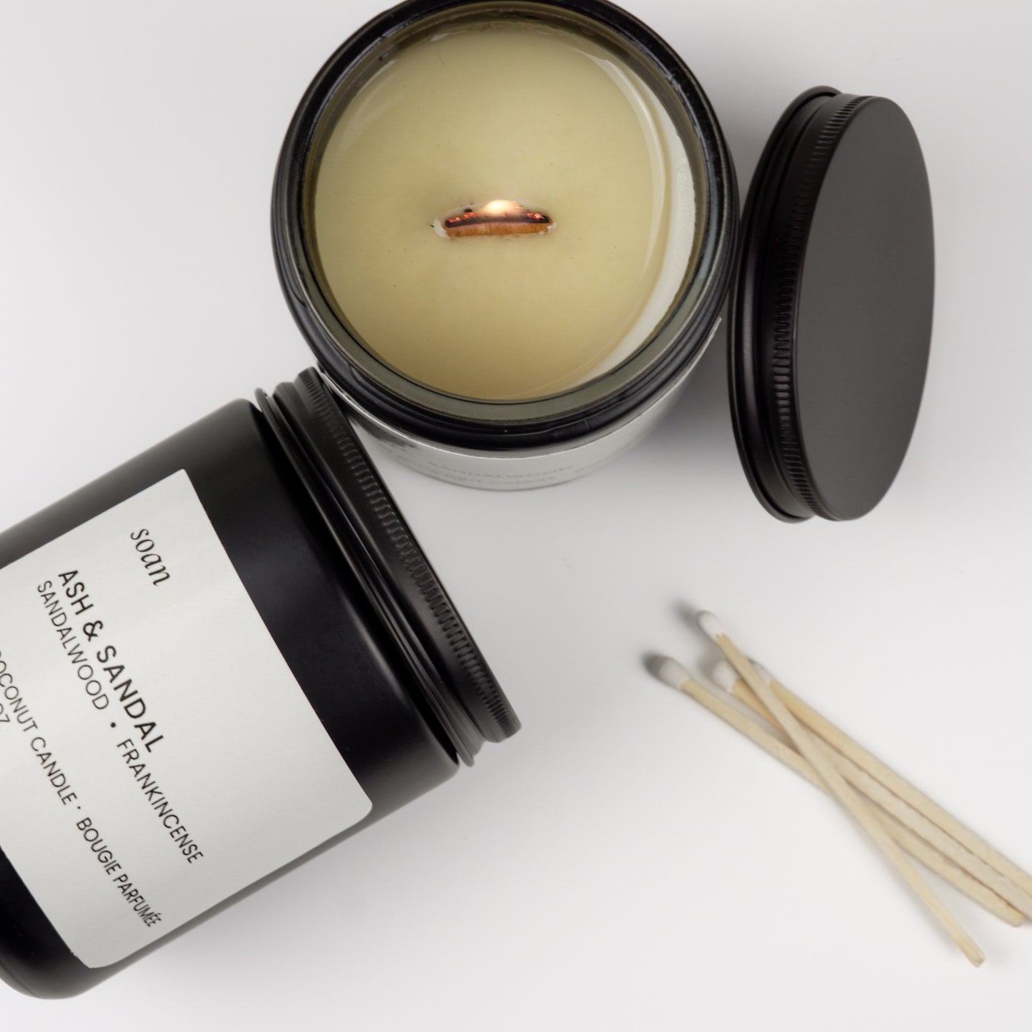 Candle with open lid, matches, and black container on a white background