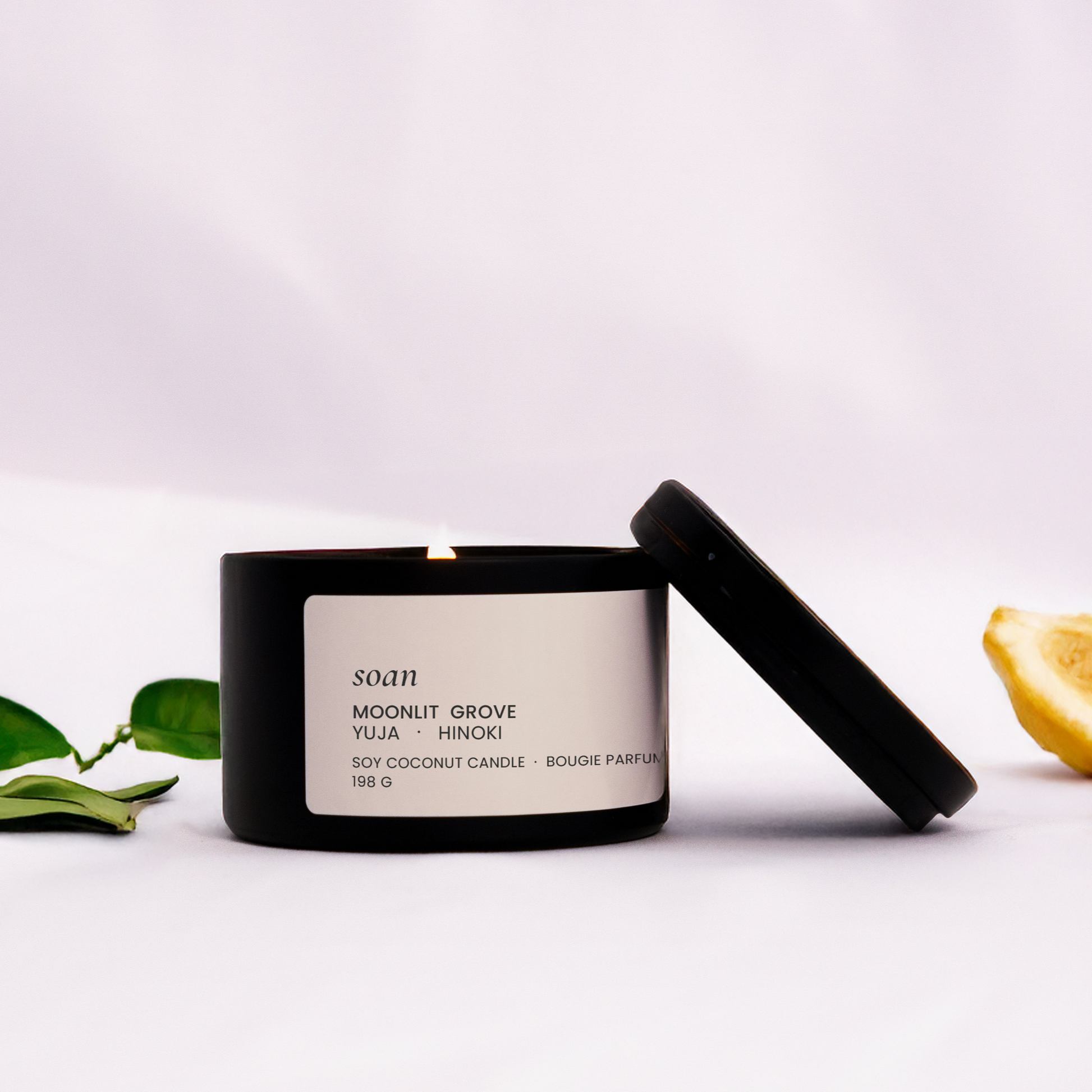 Candle with a black lid on a white surface with green leaves and lemons.