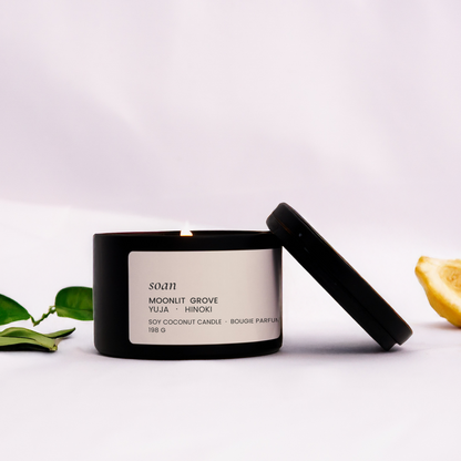 Candle with a black lid on a white surface with green leaves and lemons.
