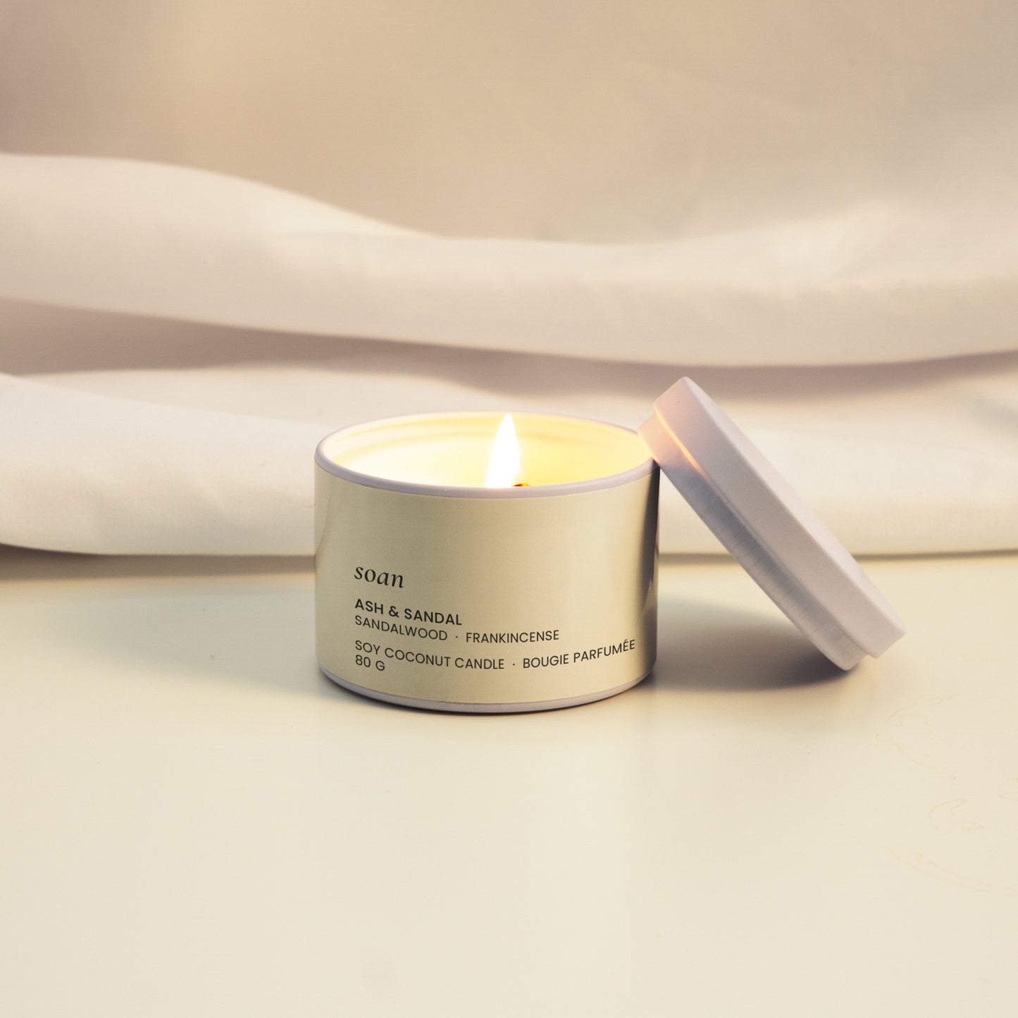 Candle in a silver tin with a white label on a light fabric background