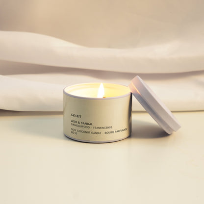 Candle in a silver tin with a white label on a light fabric background