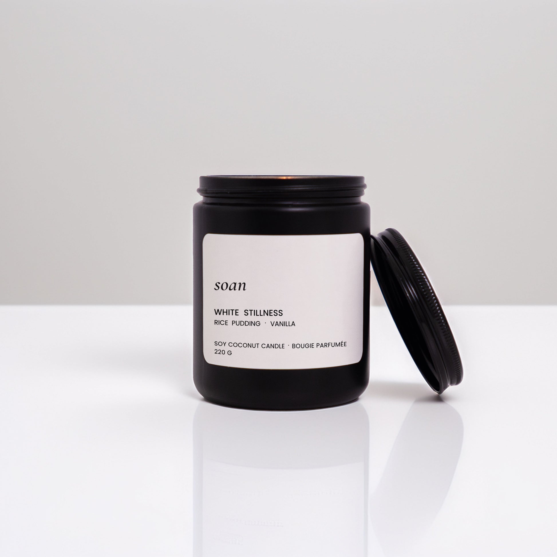 Black candle jar with a white label on a reflective surface