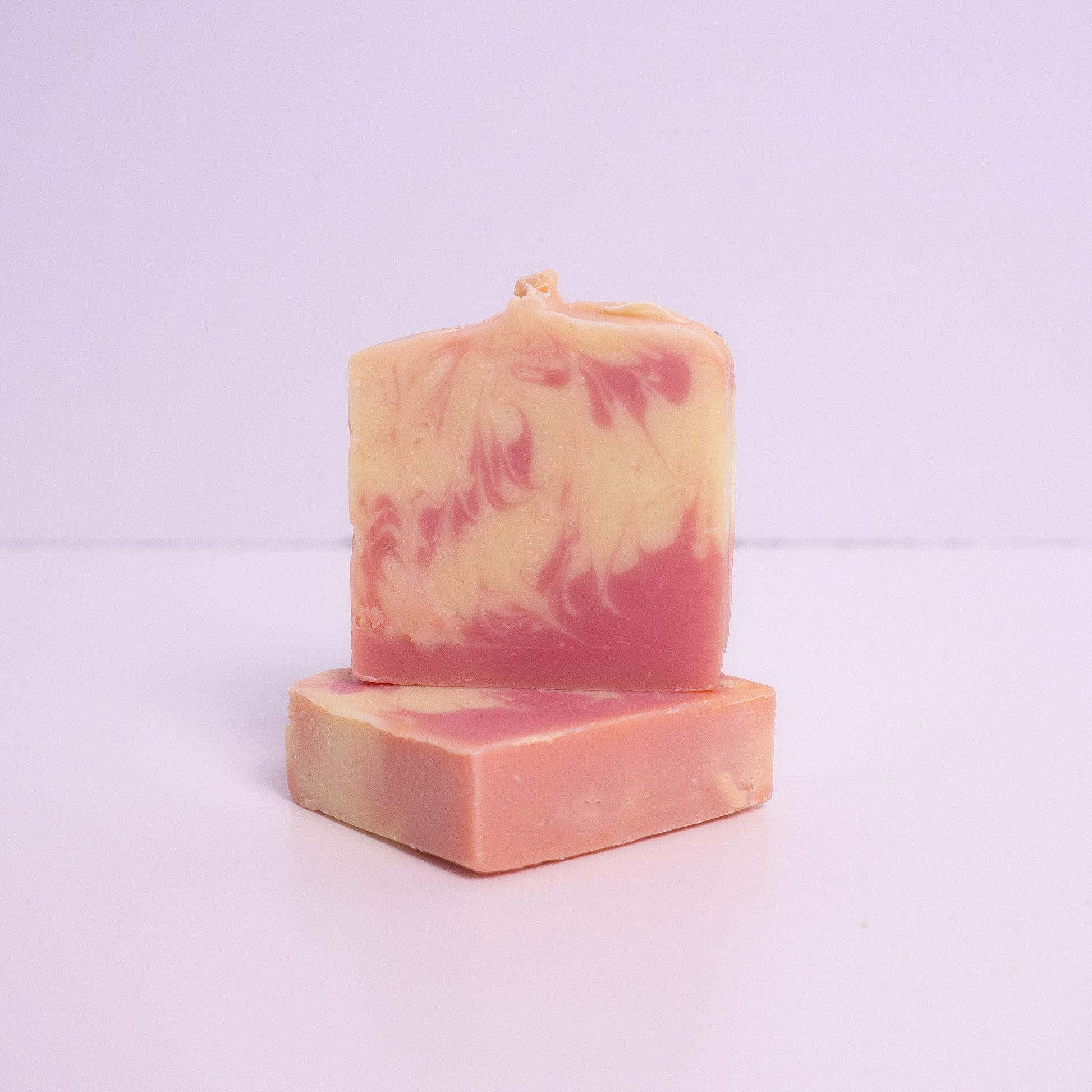 Two pink and purple artisan soap bars on a light purple background