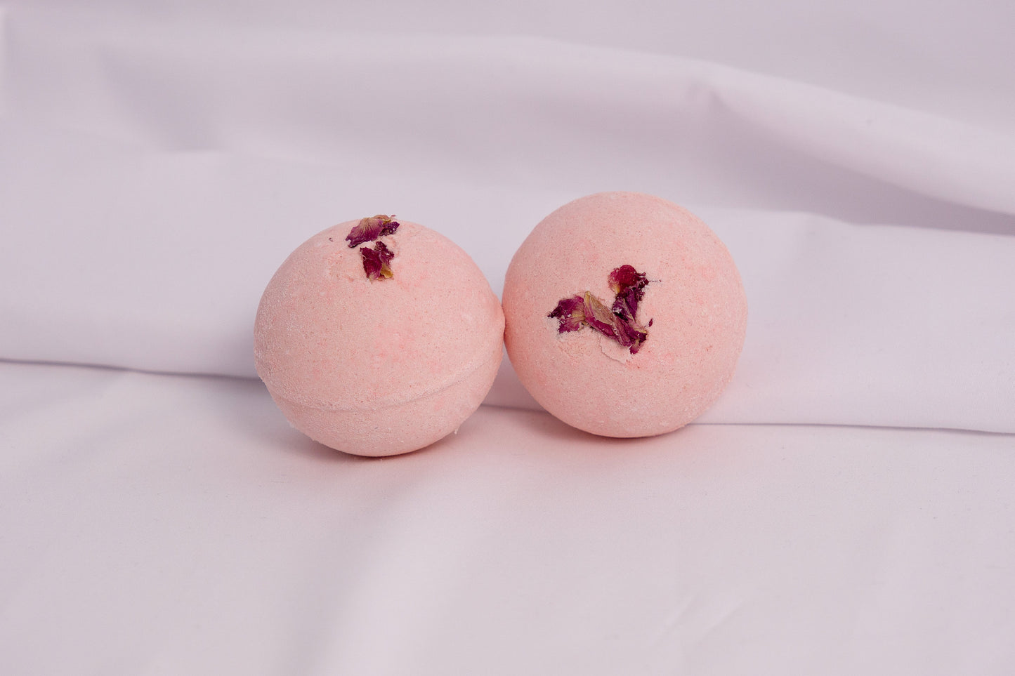 Fizzing rose bath bomb in warm water, releasing soft bubbles and a classic rose scent for a calming soak