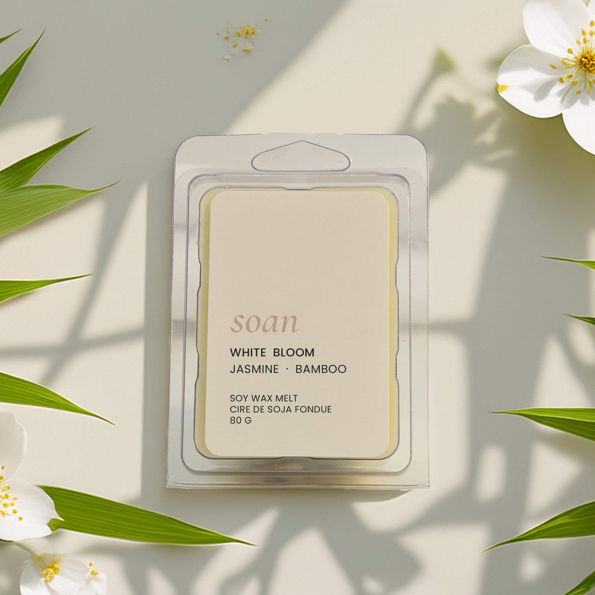 Packaged wax meltwith 'White Bloom' fragrance surrounded by white flowers and green leaves on a light background