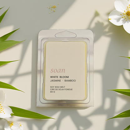 Packaged wax meltwith 'White Bloom' fragrance surrounded by white flowers and green leaves on a light background