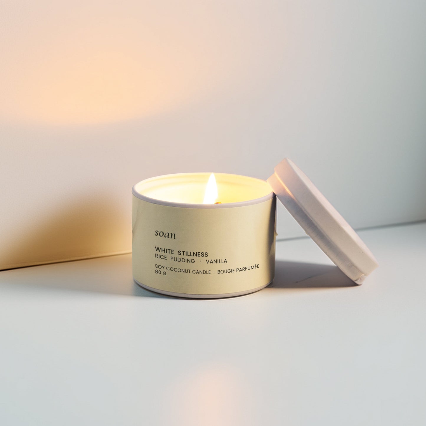 Candle in a white container with a white lid on a light surface.