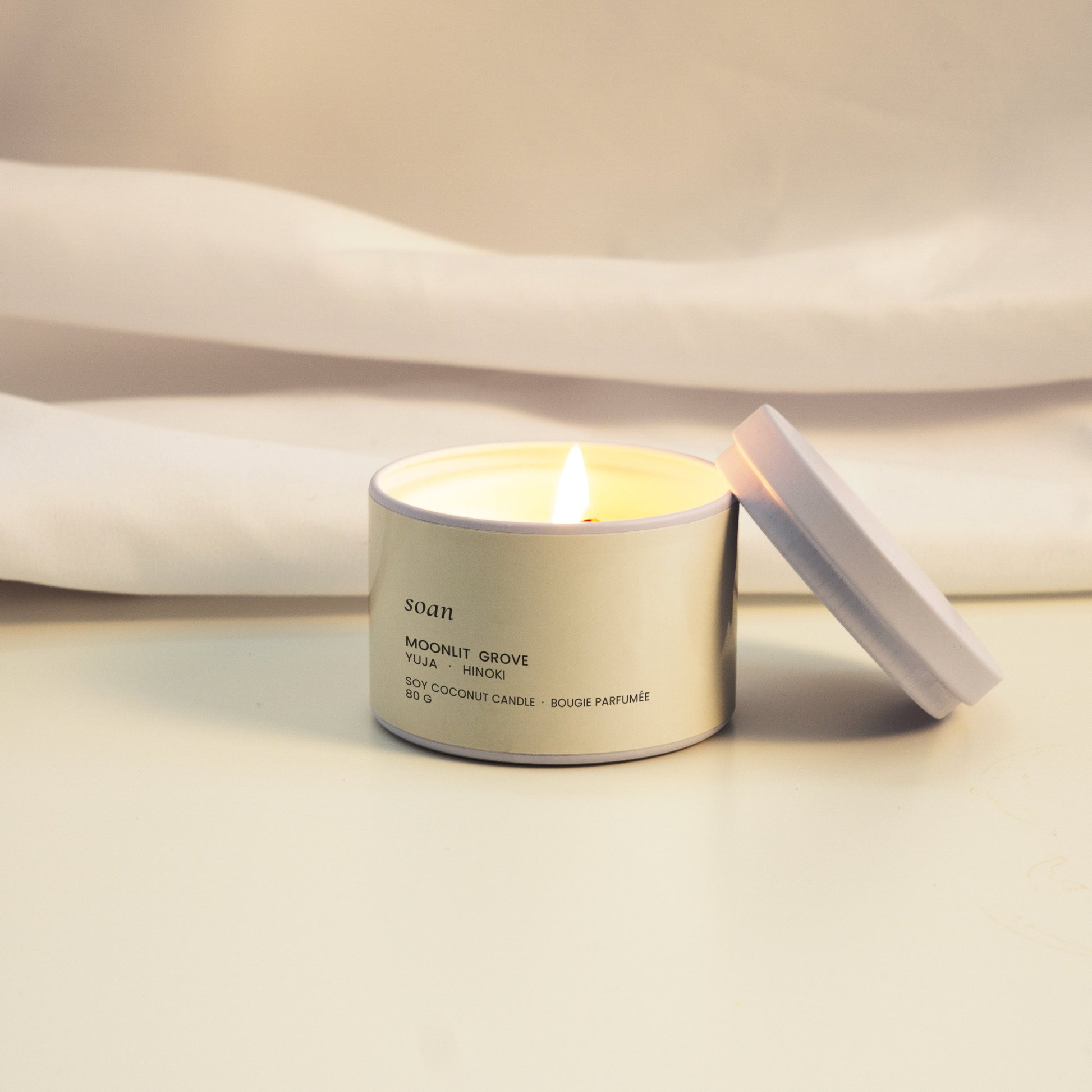 Candle in a metallic container with a white label on a light fabric background